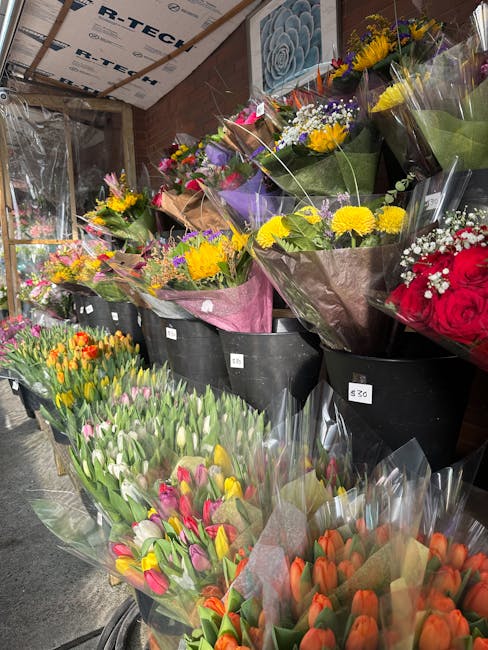 An indoor display of fresh flower bouquets arranged in black buckets, featuring vibrant tulips in shades of pink, orange, and purple, alongside smaller bouquets of yellow and purple flowers wrapped in