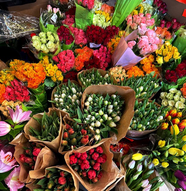 A vibrant display of fresh floral bouquets arranged closely together, featuring a variety of colorful flowers including pink and white roses, yellow and orange tulips, red and pink carnations, and whi