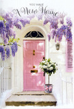 A gentle, celebratory mood surrounds this Ickenham doorway, where flowers and colour quietly honour the start of a new life in a new home. The focal point is a pastel pink front door, delicately painted and softly glowing against simple whitewashed walls, evoking the welcoming facades that line the residential streets near Long Lane or around Ickenham Station. Above and around the door, cascades of wisteria in muted lavender and lilac spill down from unseen supports, their blossoms hanging in graceful, pendulous clusters that form a loose, floral canopy. These wisteria strands create a dreamy frame, with the light catching the petals and casting the sort of soft, patterned shadows you might notice on a mild spring afternoon. At the doorstep, a grey tin bucket rests as an impromptu vase, brimming with an abundant bouquet of creamy white roses. The roses are fat and full, their multi-layered petals unfolding in soft spirals, each bloom pressed gently against the next to create a plush, cloud-like effect. Fresh green foliage peeks between the blooms, adding little flickers of colour and structure. Around the base of the bucket, a pink ribbon has been tied with care, its shade harmonising perfectly with the front door and bringing the entire arrangement into cohesive, pastel balance. The overall scene feels intimate and hopeful, like a quiet lane just off the main roads where a family is unpacking and neighbours might soon drop by. It is an image that speaks of housewarming wishes, thoughtful congratulations, and the simple comfort of arriving somewhere that immediately feels like home.